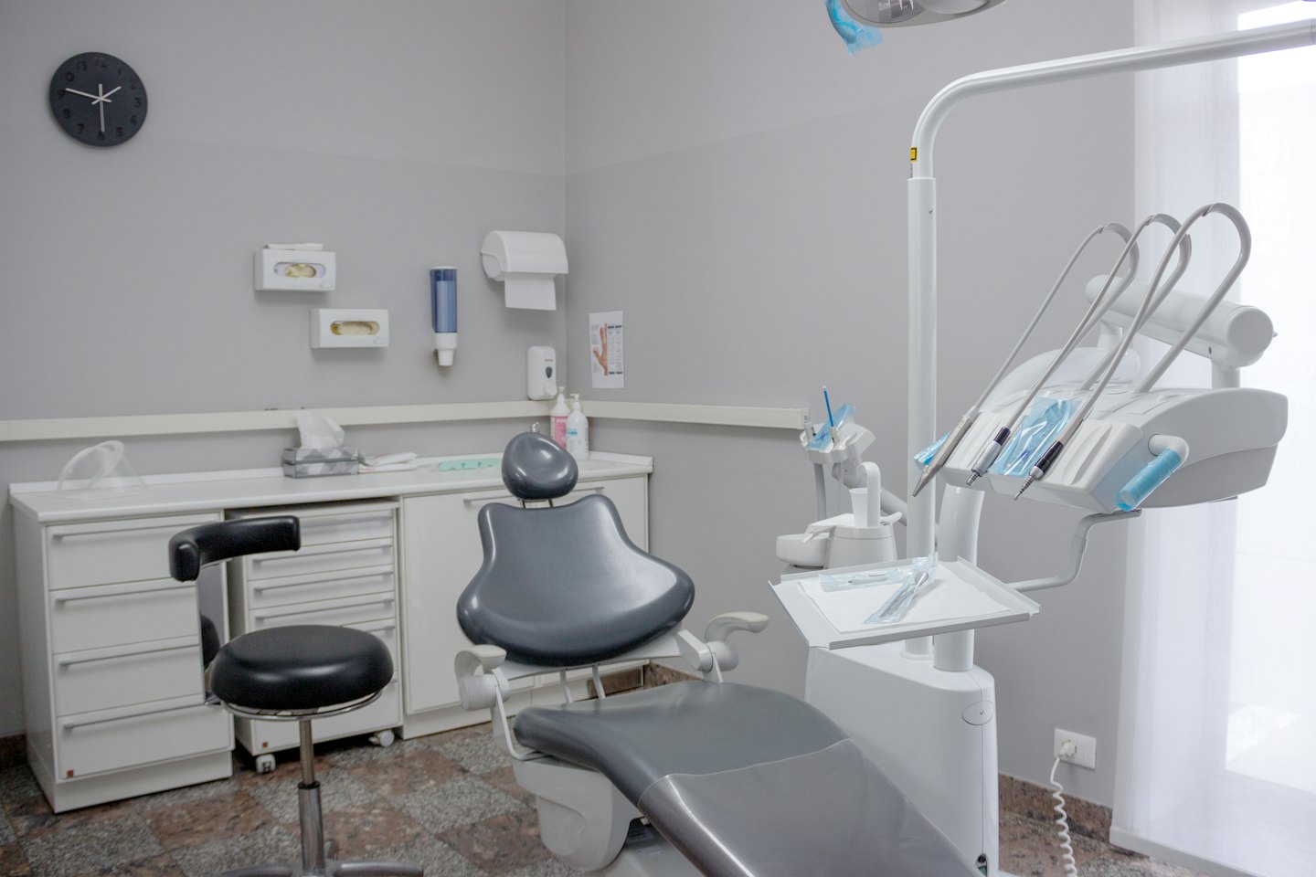 Consultorio dental moderno y vacío con silla gris y equipo blanco.