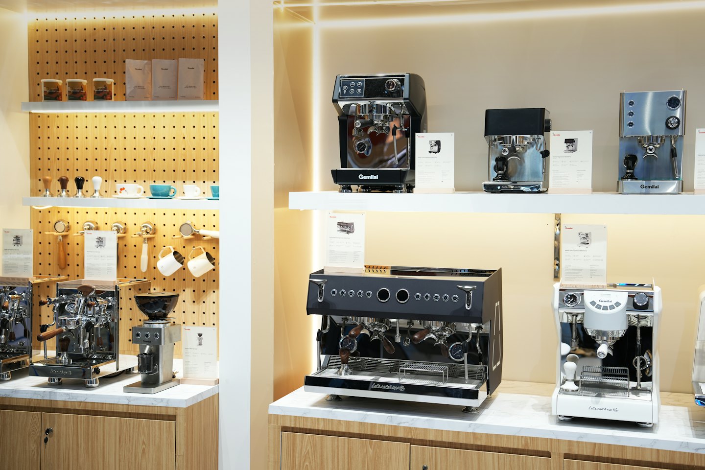 Máquinas de espresso y accesorios de café expuestos en estantes y tableros perforados.